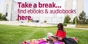 Person sitting on lawn with a tablet in front of the Information Commons